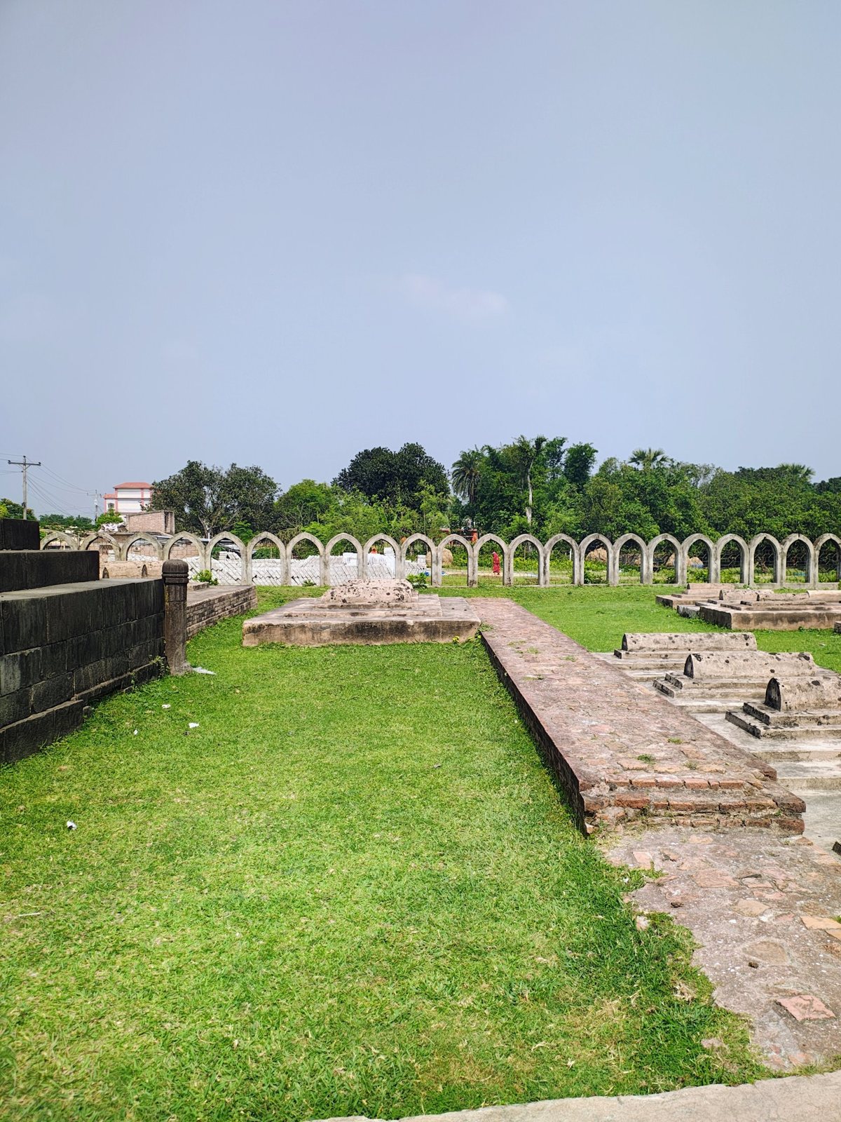 Historic stepped graves on a green lawn in front of pointed arches near Sona Masjid, Chapainawabganj