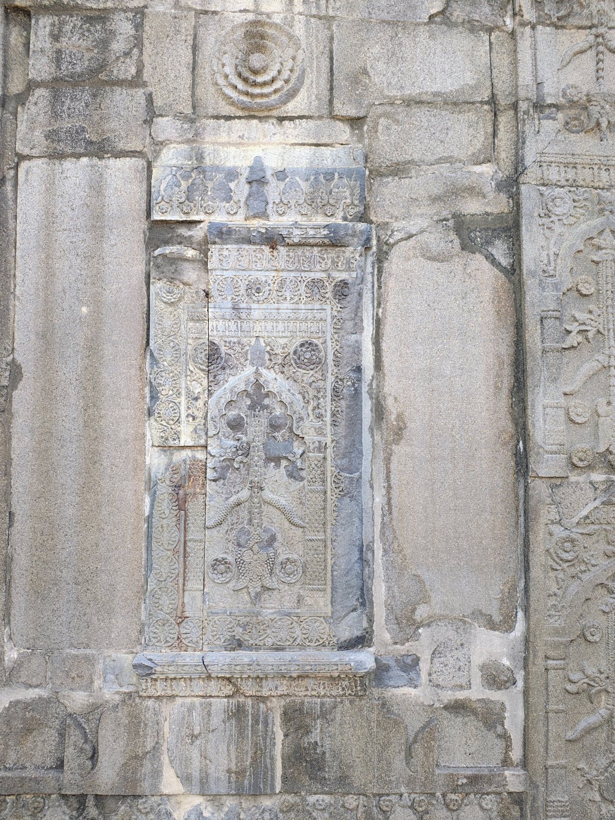Weathered carved stone panel with rosette and hanging-lamp motif at Sona Masjid
