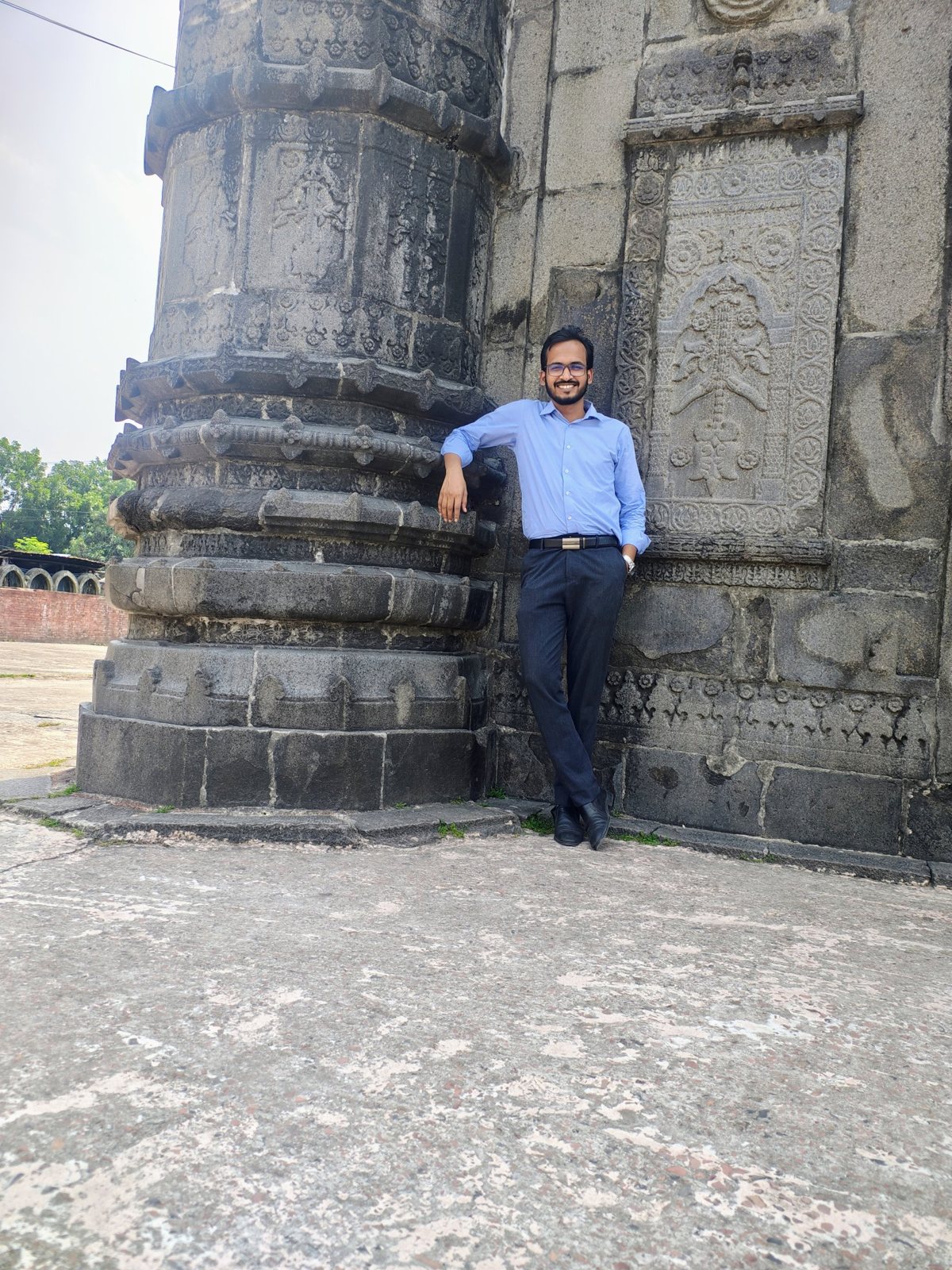 Sayedul Abrar beside a carved dark-stone corner pillar at Sona Masjid in Shibganj, Chapainawabganj