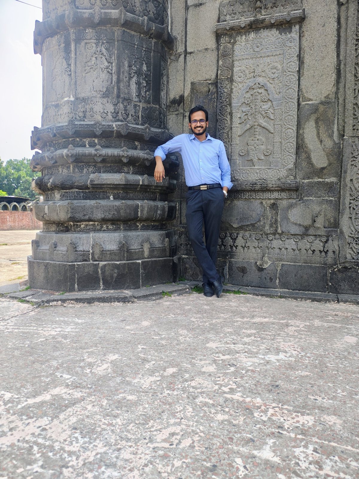 Sayedul Abrar smiling beside an ornate stone pillar and wall panels at Sona Masjid, Chapainawabganj